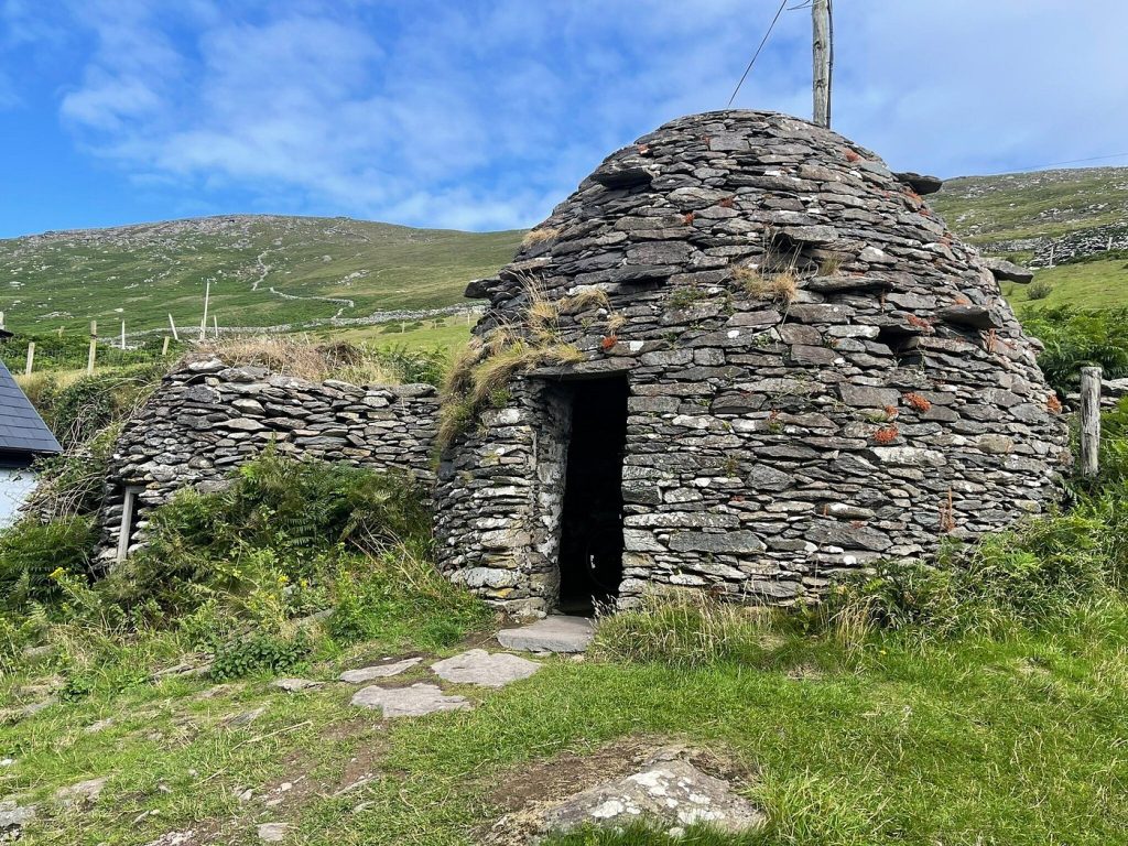 Stone hut with grass roof on a sunny hillside with blue skies.